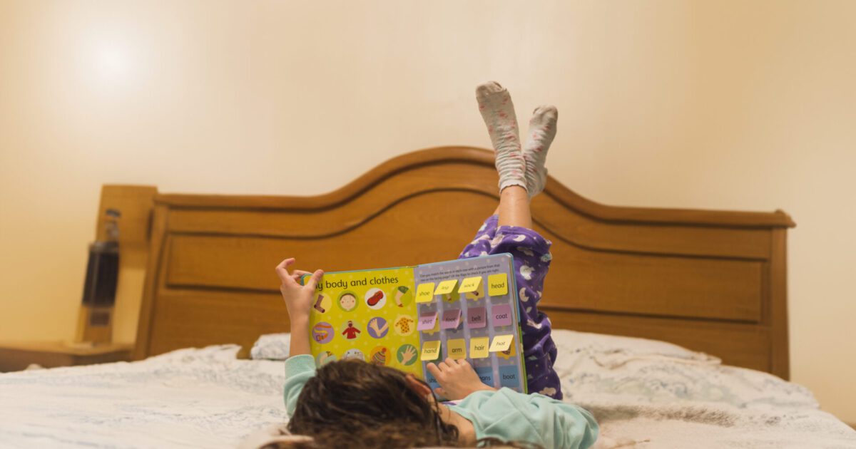 Criança deitada na cama explorando livros sensoriais