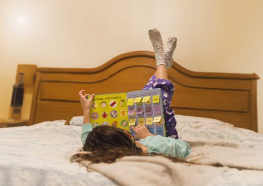 Criança deitada na cama explorando livros sensoriais